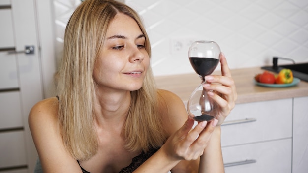 La mujer mira el reloj de arena y sonríe. Ella en una cocina luminosa y espera