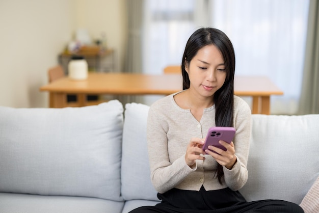 La mujer mira el teléfono móvil y se sienta en el sofá en casa