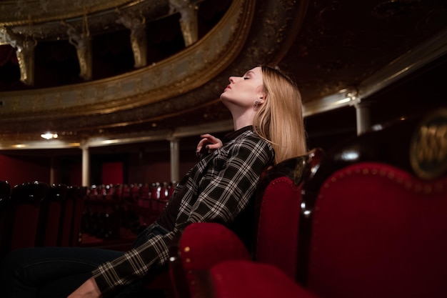 Foto mujer mirando hacia abajo mientras está sentada en el asiento del teatro de la ópera con el cabello largo y rubio