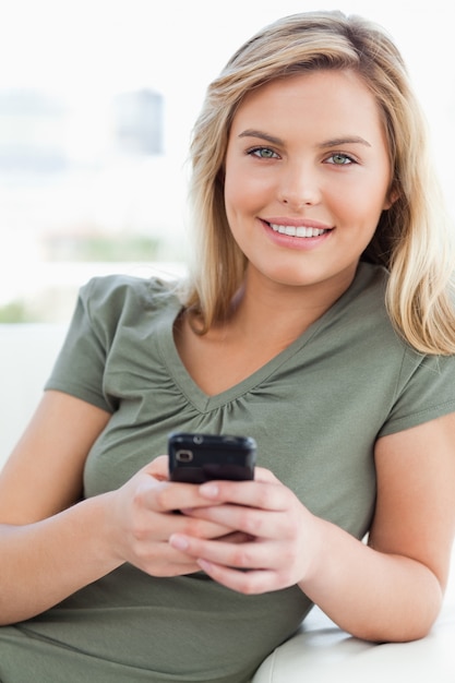 Mujer mirando hacia adelante y sonriendo mientras sostiene su teléfono