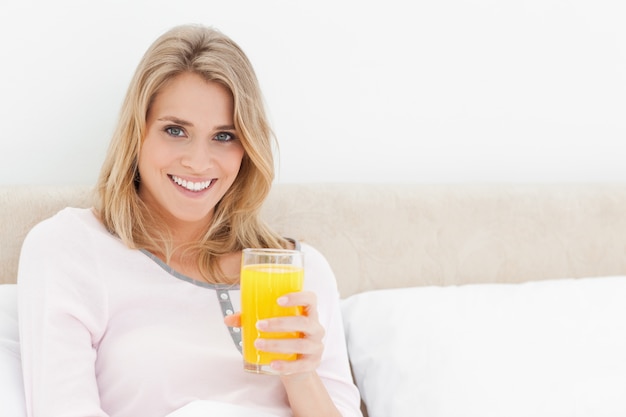 Mujer mirando hacia adelante y sonriendo con un vaso de jugo de naranja en la mano