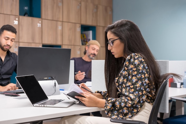 Mujer mirando la agenda mientras trabaja junto a sus colegas en un coworking