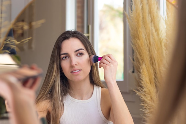 Mujer mirando al espejo mientras contornea su rostro en el proceso de maquillaje