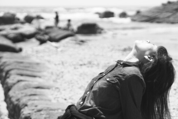 Foto mujer mirando hacia arriba mientras está sentada en la playa en un día soleado