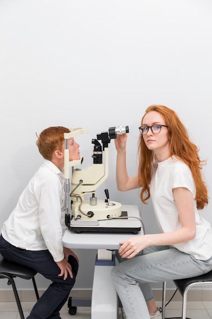 Mujer mirando a la cámara mientras revisa el ojo del niño con refractómetro