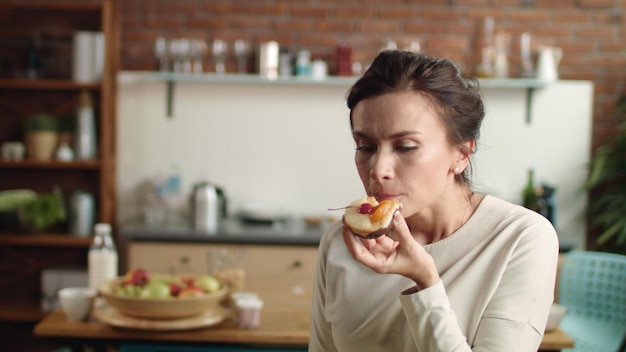 Mujer mirando a la cámara con pastel elegante en la mano Chica mordiendo el postre en casa