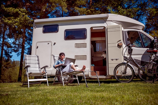 Mujer mirando la computadora portátil cerca del campamento. Vacaciones en coche caravana. Viajes de vacaciones familiares, viajes de vacaciones en autocaravana RV. Tecnología de comunicación de información de conexión Wi-Fi.