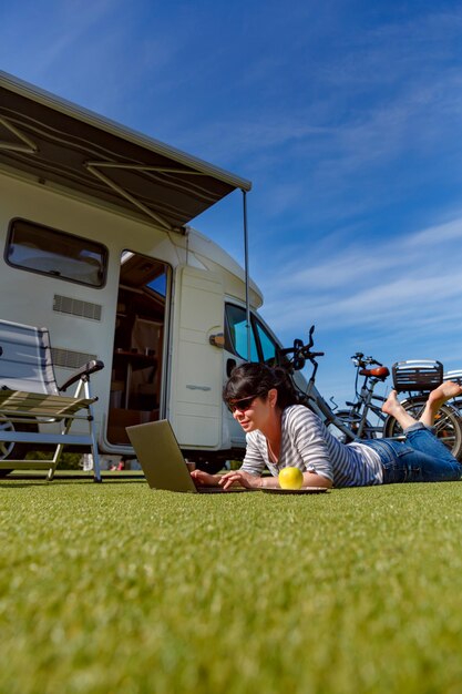 Mujer mirando la computadora portátil cerca del campamento. Vacaciones en coche caravana. Viajes de vacaciones familiares, viajes de vacaciones en autocaravana RV. Tecnología de comunicación de información de conexión Wi-Fi.