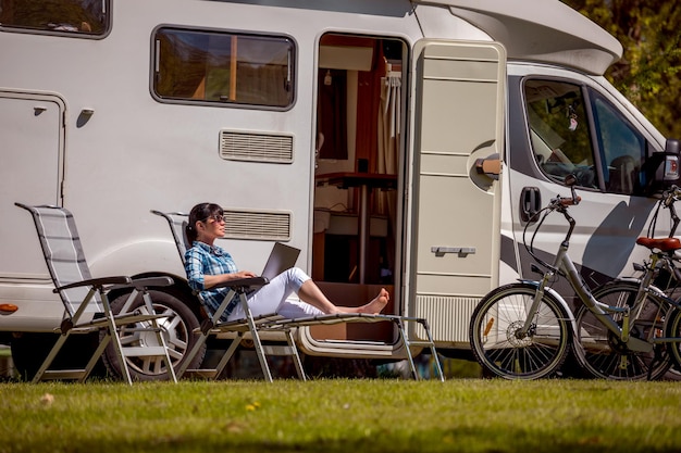 Mujer mirando la computadora portátil cerca del campamento. Vacaciones en coche caravana. Viajes de vacaciones familiares, viajes de vacaciones en autocaravana RV. Tecnología de comunicación de información de conexión Wi-Fi.