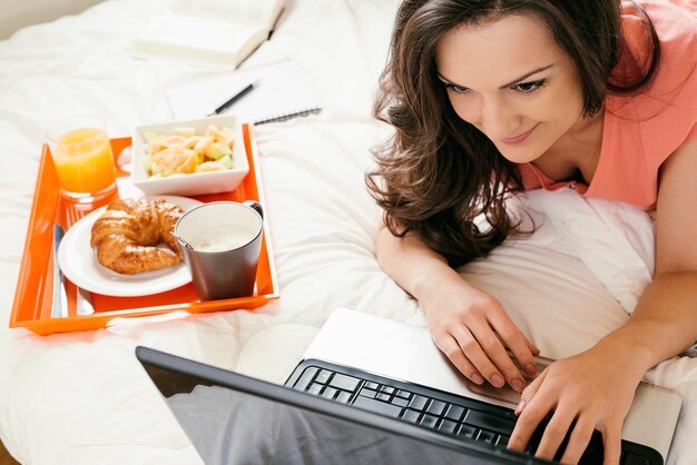 Mujer mirando la computadora portátil y desayunando