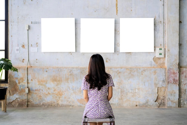 Mujer mirando marco de fotos en blanco en la galería de arte de pared blanca