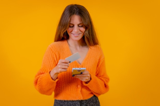 Mujer mirando pagar con tarjeta en internet en compras en línea de fondo amarillo de teléfono móvil