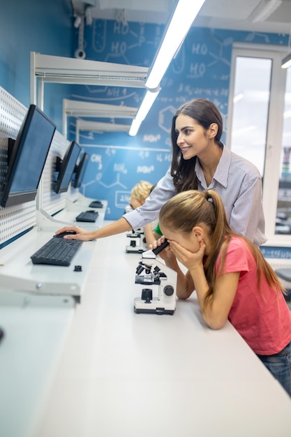 Mujer mirando la pantalla y niña inclinada sobre el microscopio