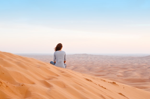 Mujer mirando la puesta de sol en la arena del desierto