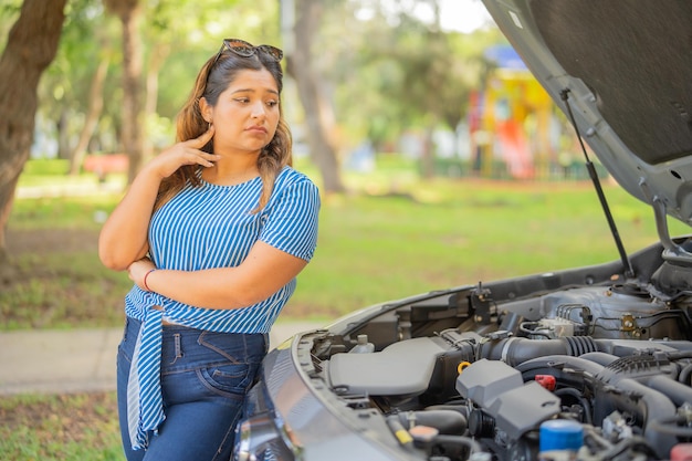 Foto mujer mirando su coche destrozado apoyándose en el vehículo