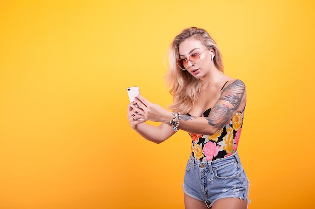 Mujer mirando su móvil con gafas sobre fondo amarillo