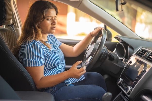 Foto mujer mirando su teléfono celular mientras conduce sosteniendo el volante con una mano