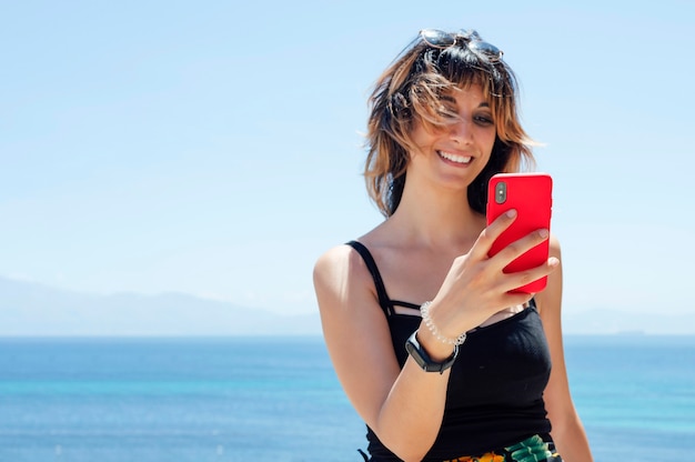 Mujer mirando el teléfono móvil con el mar de fondo