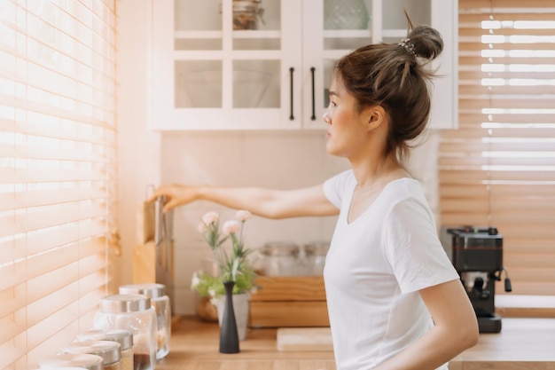 Mujer mirando por la ventana desde la cocina blanca y cálida