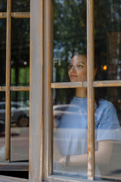 Mujer mirando por la ventana con incertidumbre Mujer pensativa mirando hacia otro lado por la ventana mientras piensa en su futuro