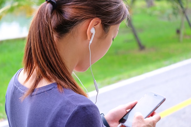 Foto una mujer mirándola un teléfono inteligente para seleccionar la música antes del ejercicio.