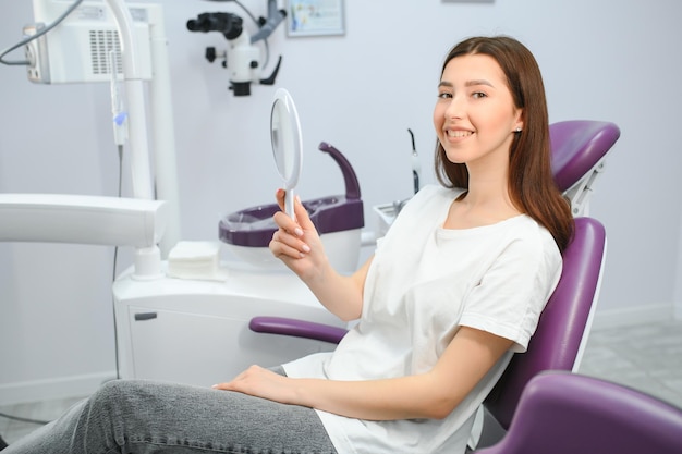 Mujer mirándose en el espejo y sonriendo después de un chequeo en el consultorio del dentista