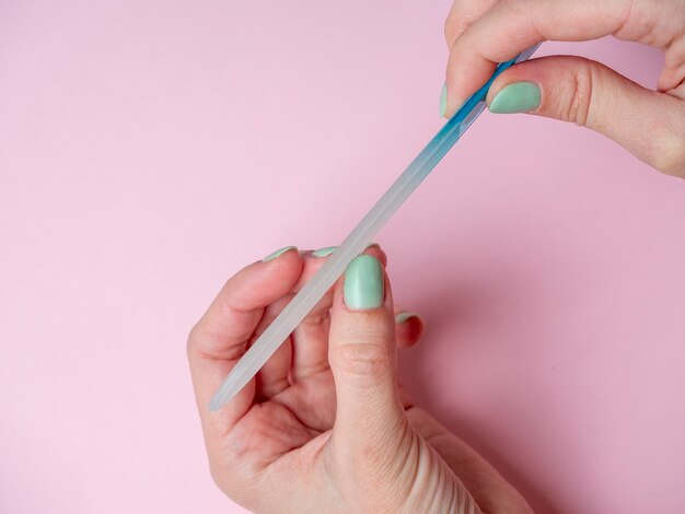 Una mujer misma se está limando las uñas con una lima de uñas en la mano sobre un fondo rosa. Cuidado de las uñas a mano en casa. Belleza y salud