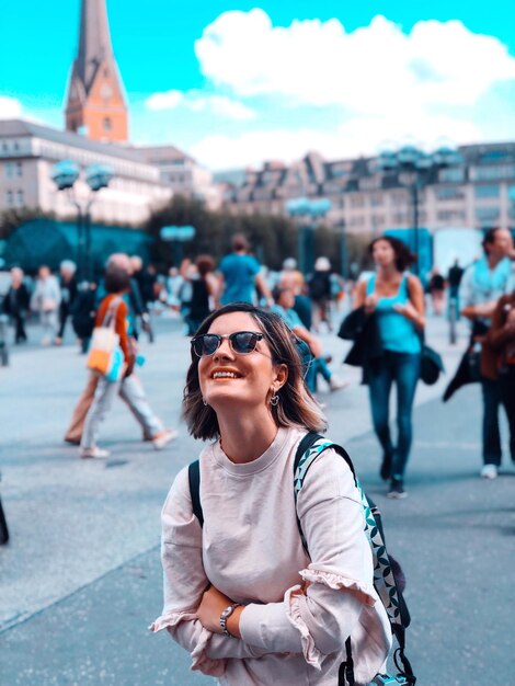 Foto una mujer de mochila adulta sonriente de pie en la calle de la ciudad