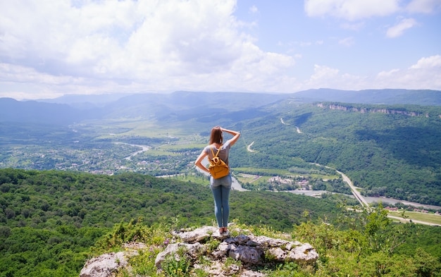 Mujer con una mochila amarilla mirando una hermosa vista desde la montaña
