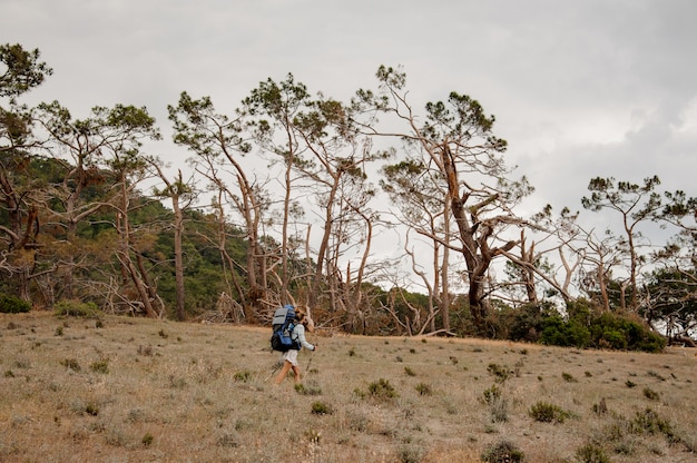 Mujer con mochila y bastones caminando por el campo seco