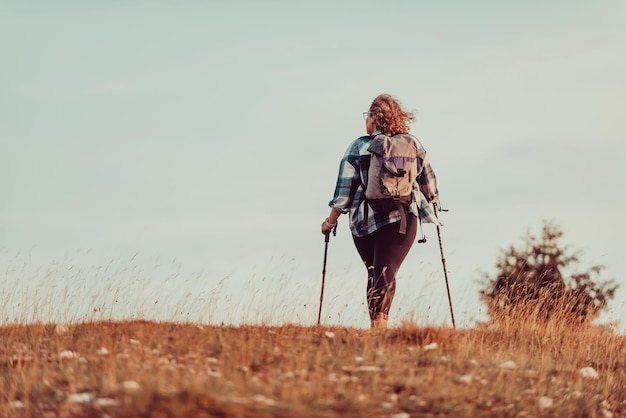 Una mujer con una mochila en la espalda y equipo de montañismo caminando en la cima de una montaña al atardecer