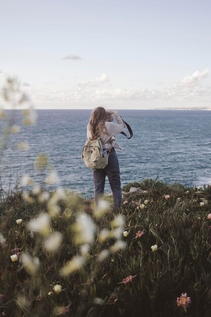 Foto mujer con mochila de pie junto al mar contra el cielo