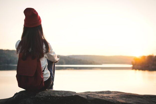 Foto mujer con mochila sentada junto al lago contra un cielo despejado