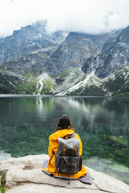 Mujer mochilera sentada en una roca disfrutando de la vista del lago en las montañas del parque nacional tatra