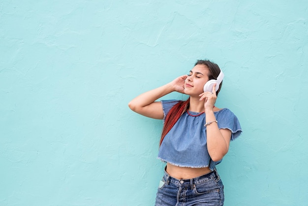 Mujer de moda alegre con el pelo rojo escuchando la música en el fondo de la pared azul en la calle