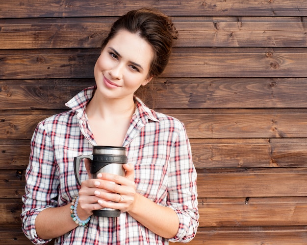 Mujer de moda alegre que sostiene el café al aire libre en fondo de madera