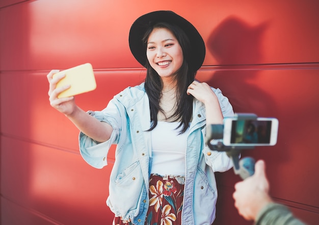 Mujer de moda asiática vlogging mientras usa el teléfono inteligente al aire libre. Niña china feliz divirtiéndose con tecnología de nuevas tendencias