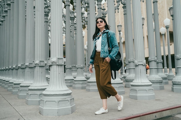 mujer de moda con chaqueta de jean con pañuelo para el cuello y caminando por el museo de arte del condado de Los Ángeles