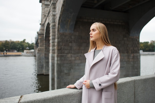 Mujer de moda con estilo elegante joven en abrigo gris en el puente europeo clásico mirando hacia afuera