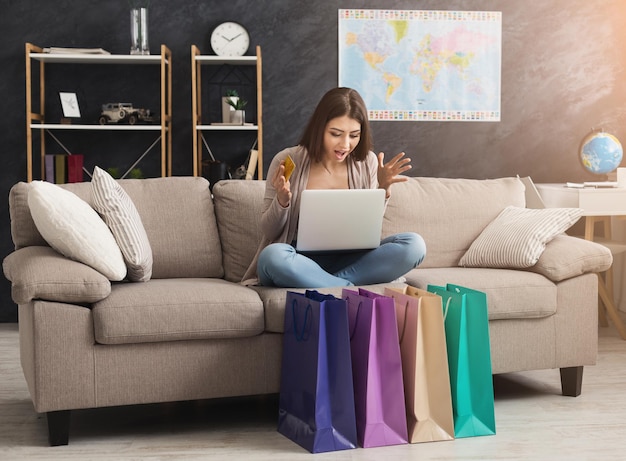 Mujer de moda feliz comprando en línea con computadora portátil y tarjeta de crédito, con coloridas bolsas de compras, espacio de copia