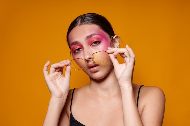 Mujer de moda gafas de moda maquillaje de cara rosa posando aspecto atractivo fondo amarillo inalterado