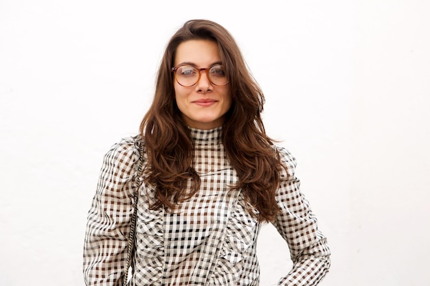 Mujer de moda con gafas de pie junto a la pared blanca