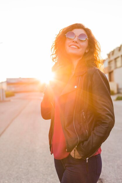 Mujer de moda con gafas de sol en la carretera durante la puesta de sol