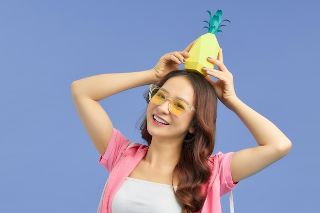 Mujer de moda en gafas de sol con piña en la cabeza sobre fondo azul.