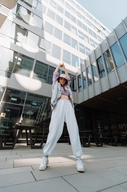 Mujer de moda con gafas de sol y sombrero bailando afuera mirando a la cámara bailarina femenina