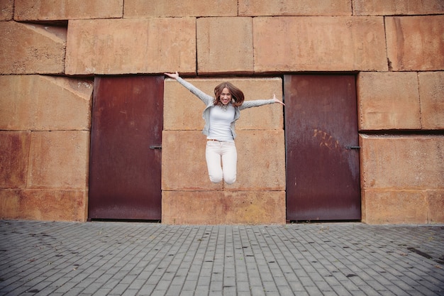 Mujer de moda joven feliz saltando delante de la pared de piedra