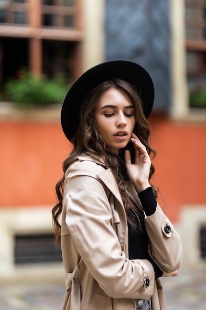 Mujer de moda joven con sombrero y abrigo posando en la calle.