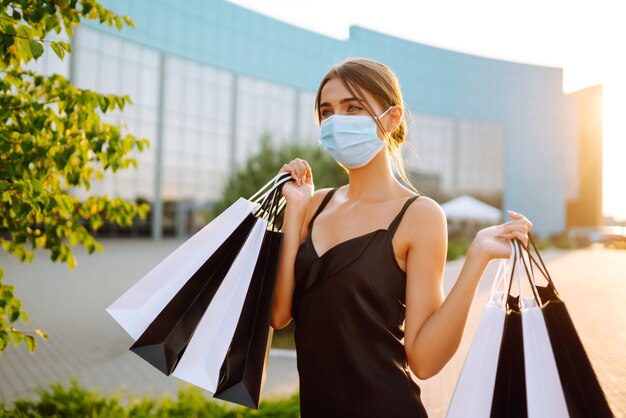 Mujer de moda con máscara médica protectora con bolsas de compras al atardecer.