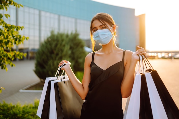 Mujer de moda con máscara médica protectora con bolsas de compras al atardecer.