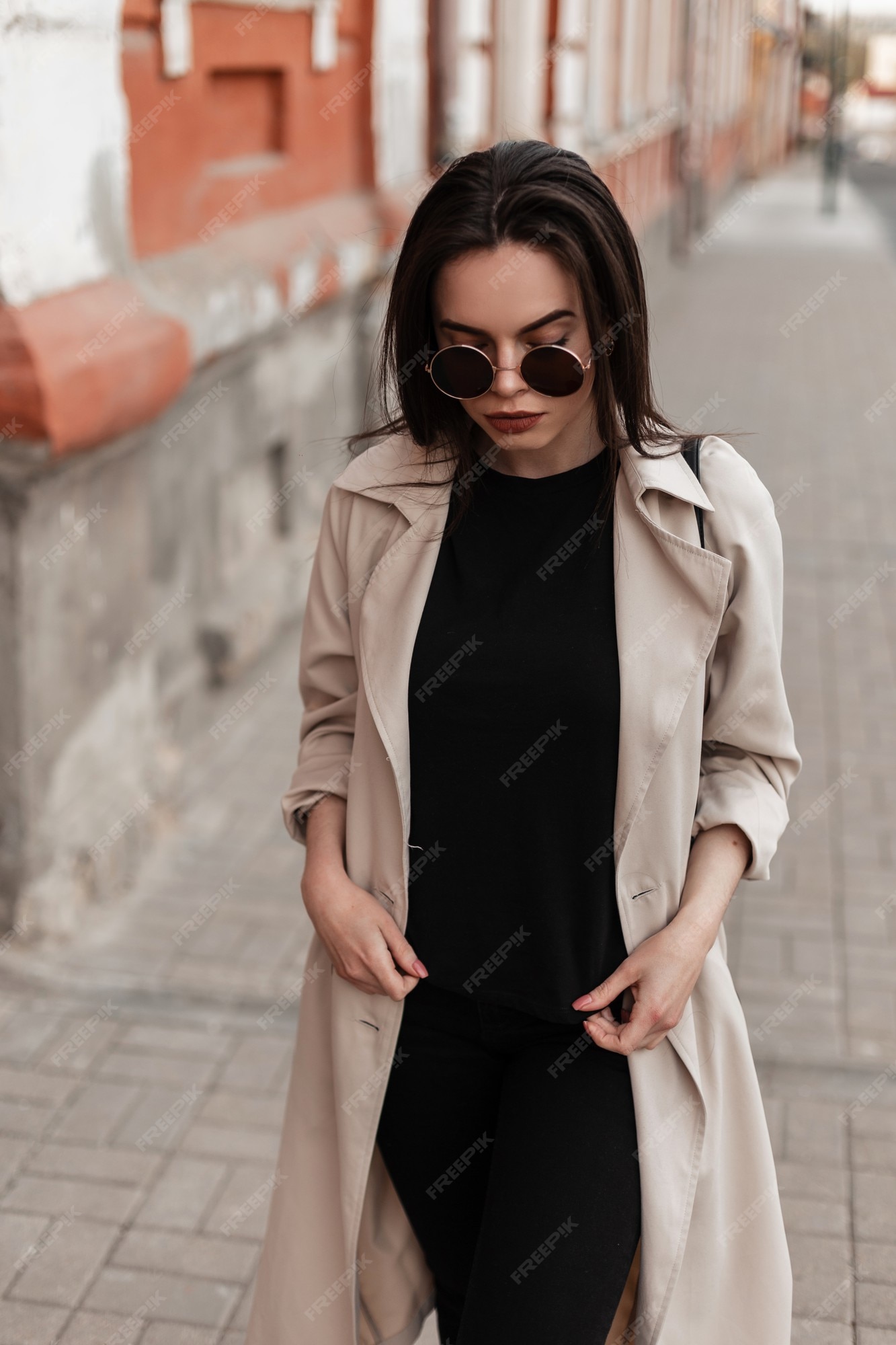 Mujer de moda de moda con gafas de sol de moda en un abrigo beige ropa negra está caminando por la calle. hermosa chica con estilo en una camiseta negra y